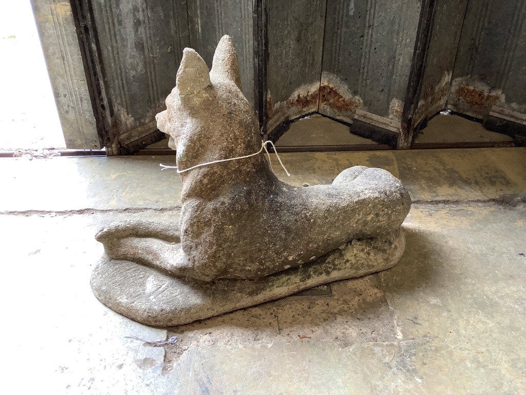 A reconstituted stone garden ornament of a recumbent German Shepherd dog, length 50cm